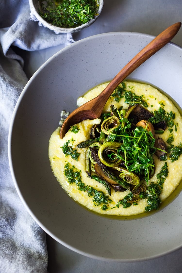 creamy polenta in bowl topped with spring veggies, pea shoots, and herby gremolata.