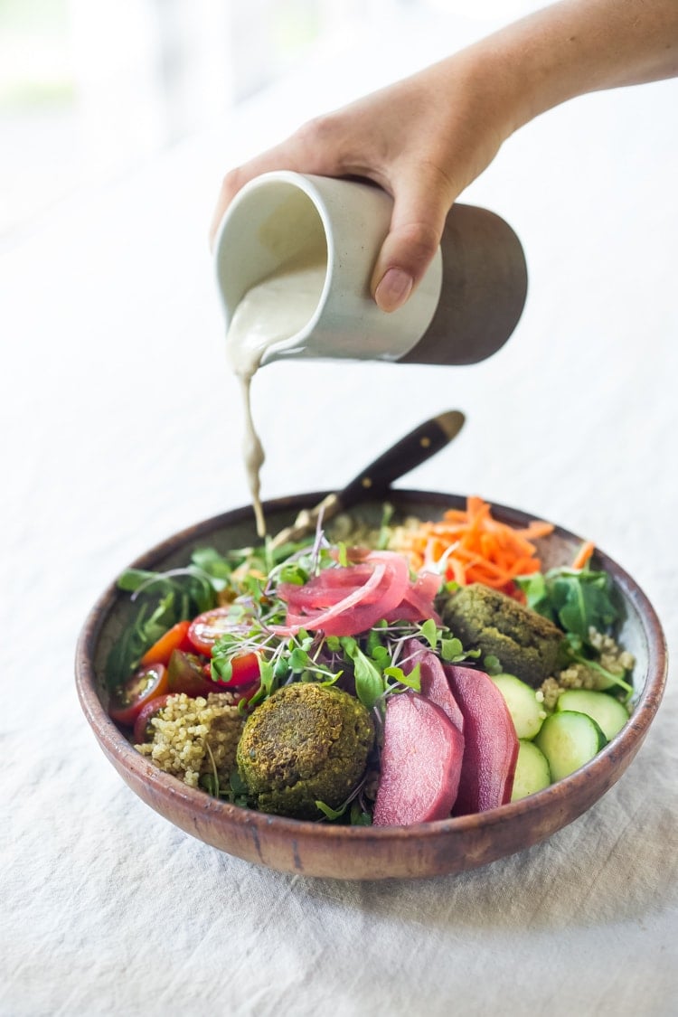 pouring tahini sauce on a falafel bowl.