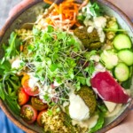 Falafel bowl with baked falafels, quinoa, lots of healthy veggies, olives, herbs and drizzled with tahini sauce.