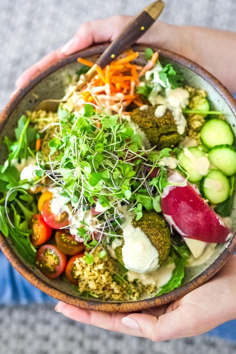 Falafel bowl with baked falafels, quinoa, lots of healthy veggies, olives, herbs and drizzled with tahini sauce.