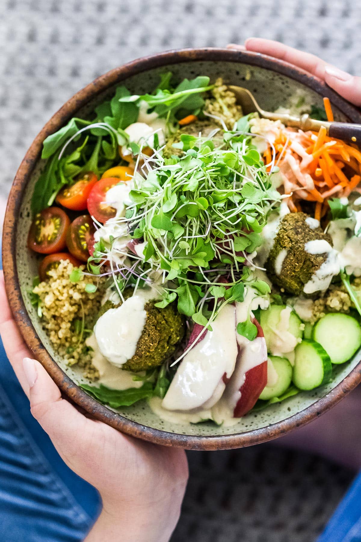 Falafel bowl with baked falafels, quinoa, lots of healthy veggies, olives, herbs and drizzled with tahini sauce.