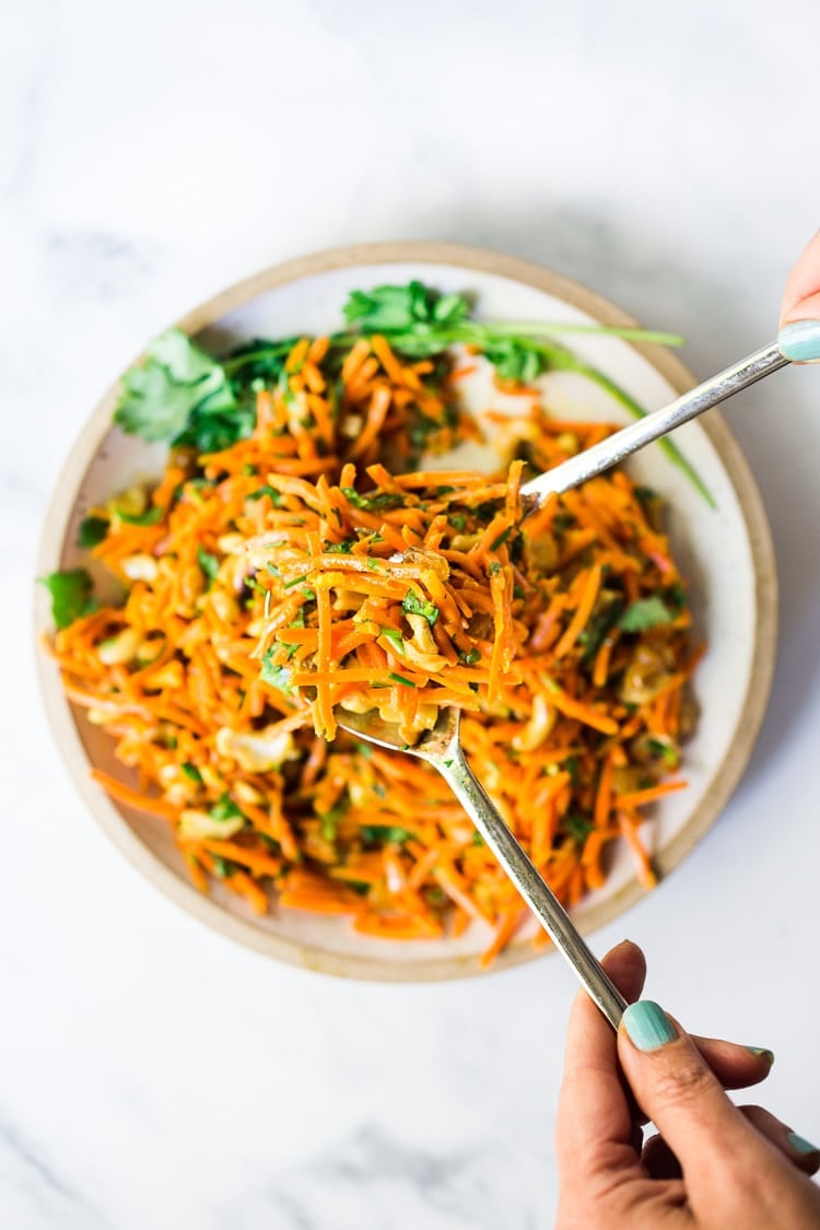 Bombay Carrot Salad with cashews and raisins, tossed in a fragrant Indian Curry dressing. Healthy and vegan this carrot salad recipe is so EASY to make, and can be made-ahead. #carrotsalad #carrotslaw #vegan #indiancarrotsalad #recipe #carrotsaladrecipe 