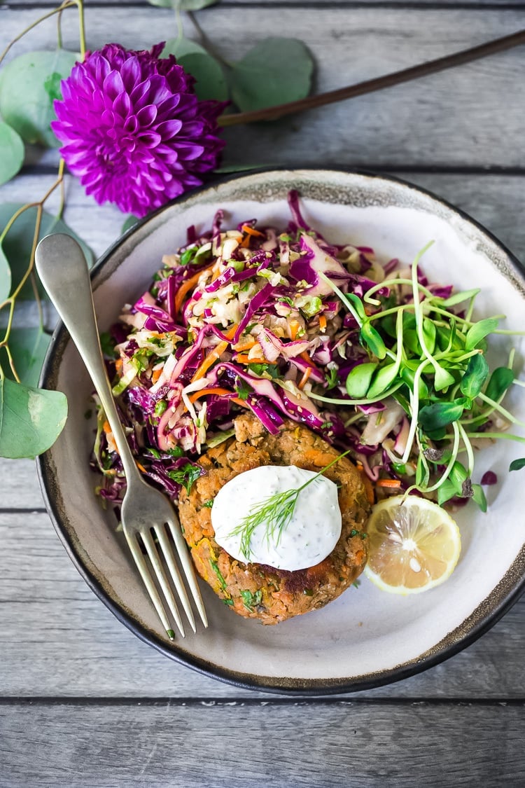 Salmoncake with dill and capers, topped with creamy dill sauce on a plate with a slaw.