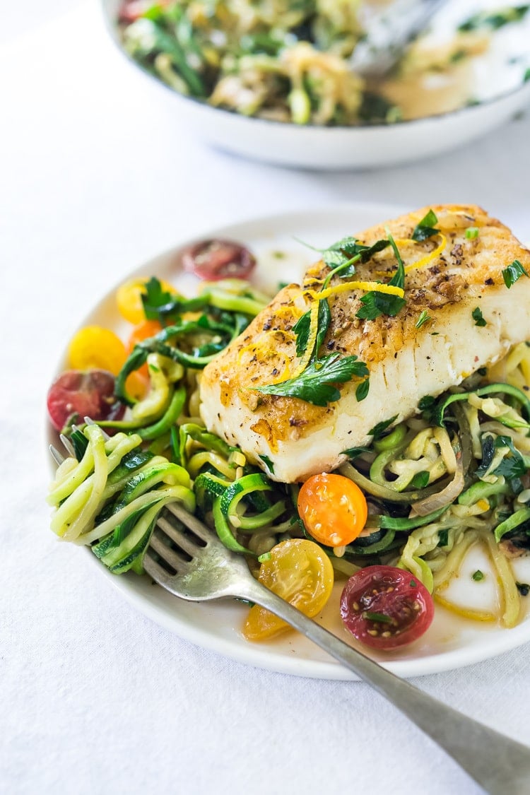 A simple, healthy Halibut recipe served over Lemony Zucchini Noodles with olive oil, garlic and parsley, topped with sweet summer tomatoes. A quick and easy low-carb meal! #keto #zucchininoodles #zoodles #halibut #halibutrecipes #lowcarb #healthy 