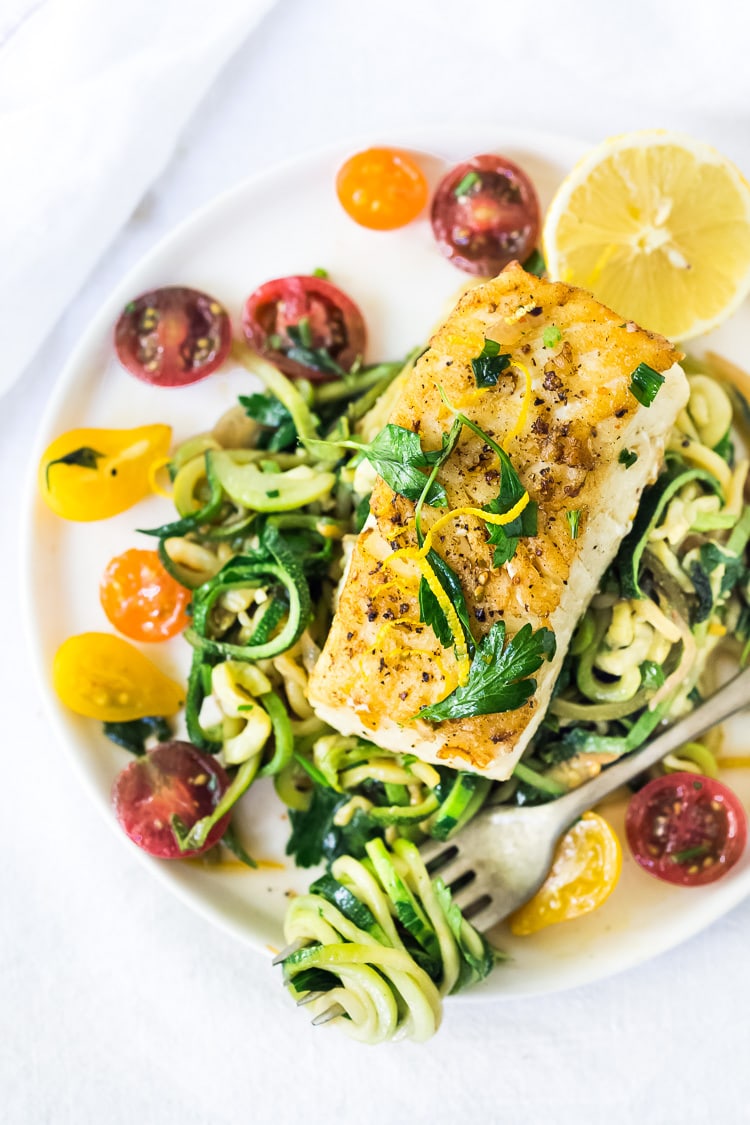 A simple, healthy Halibut recipe served over Lemony Zucchini Noodles with olive oil, garlic and parsley, topped with sweet summer tomatoes. A quick and easy low-carb meal! #keto #zucchininoodles #zoodles #halibut #halibutrecipes #lowcarb #healthy 