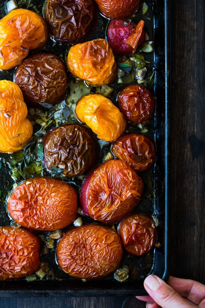 roasted tomatoes on a baking sheet with olive oil, garlic, and herbs. 