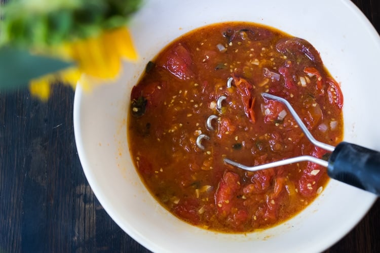 Mashing roasted tomatoes in a bowl.