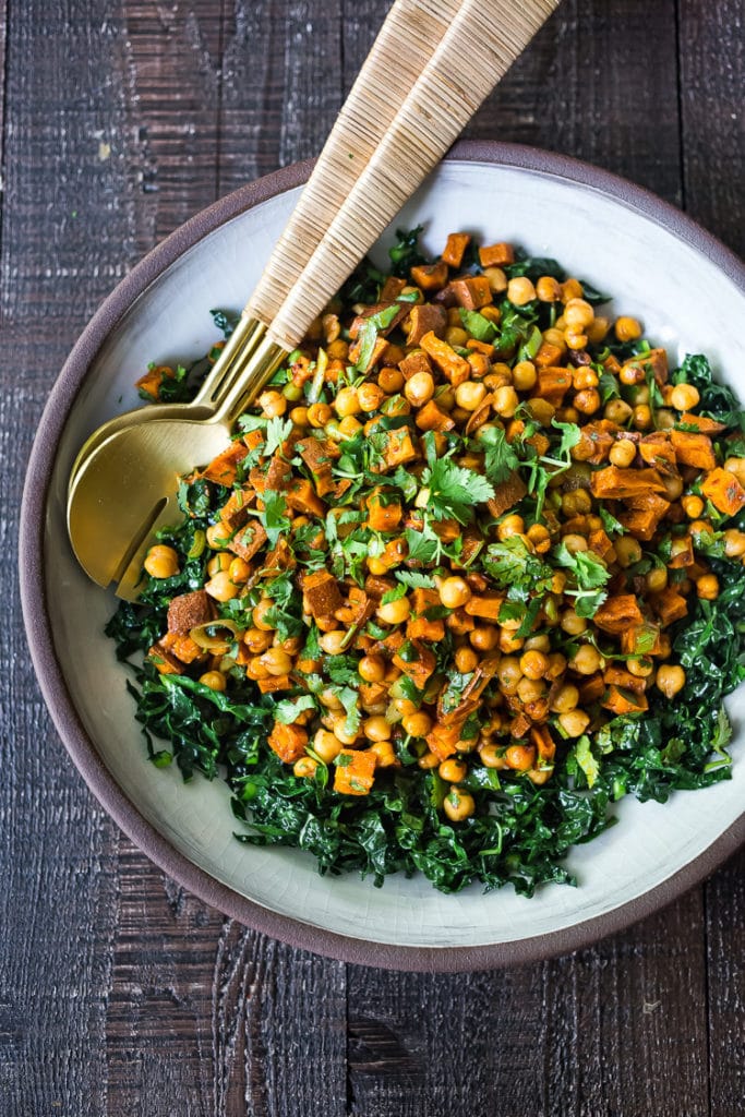 sweet potato salad with kale, chickpeas, and herbs with serving spoons. 