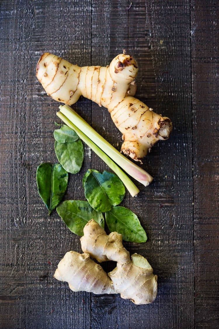 galangal root, lemongrass, kaffir lime leaves, and ginger root on wood table.
