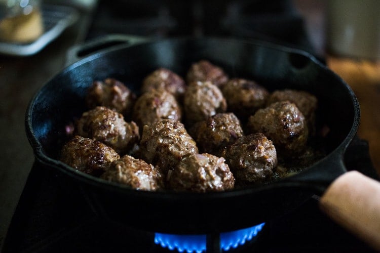 lamb meatballs searing in cast iron skillet.
