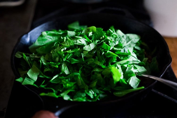 adding spinach to the mushrooms filling in a skillet.