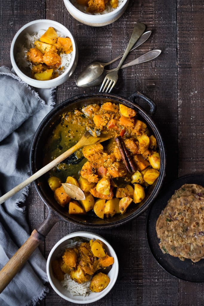 cast iron skillet with Indian butternut squash curry with potatoes, cinnamon stick, bay leaf, and wooden spoon.