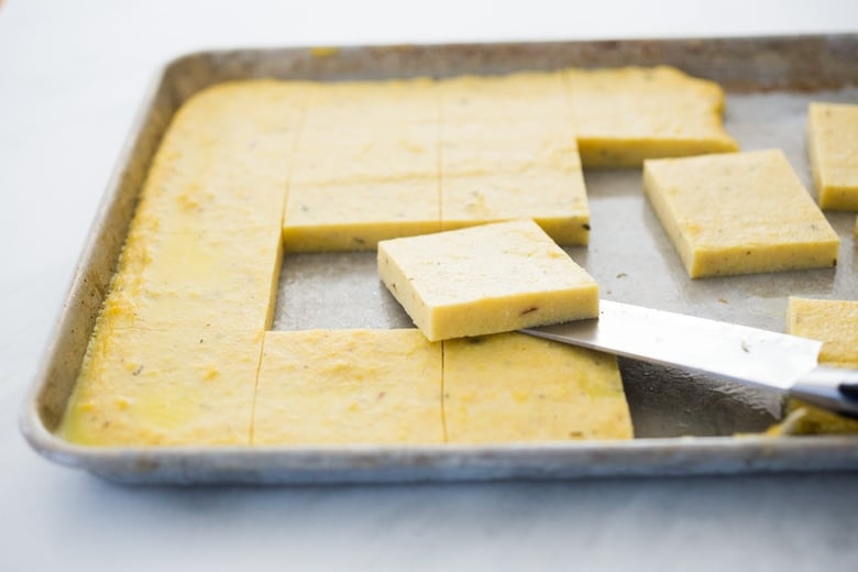 homemade firm polenta on a sheet pan, 1/2 inch thick, cut into 2 ½ inch squares.