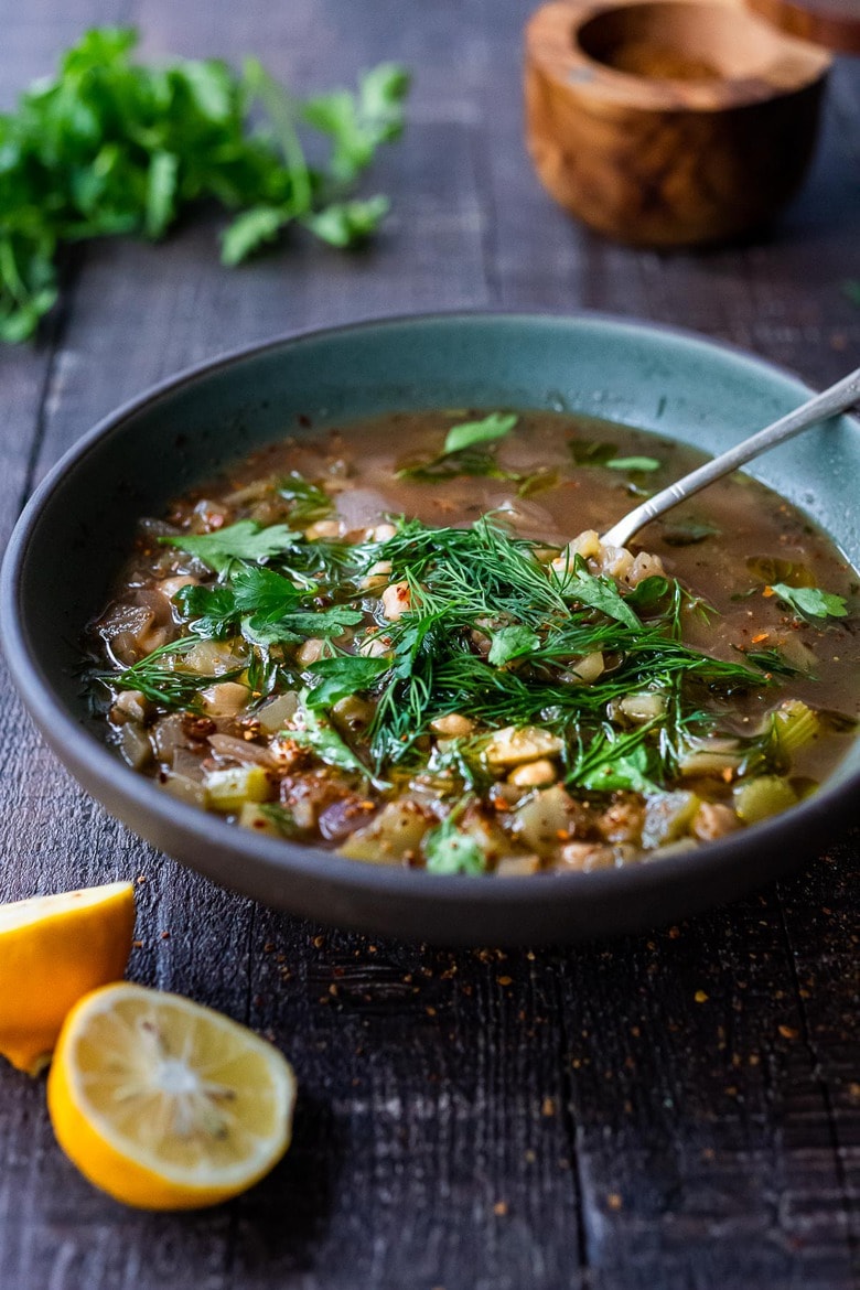 bowl of lemony chickpea soup with spoon, garnished with fresh dill and parsley.