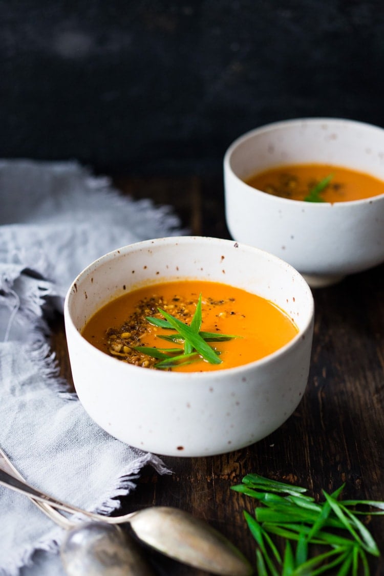 two bowls of tomato ginger soup with peanut chili crunch and sliced green onions.