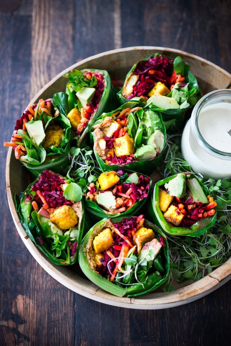 Rainbow Wraps! This vegan collard greens wraps are filled with hummus, crispy tofu, shredded beets, carrots and avocado! Drizzle with Tahini sauce! A delicious healthy lunch! #eatclean #cleaneating #vegan #veganlunch #rainbowwrap #Wraps #veganwrap #plantbased #collardgreens