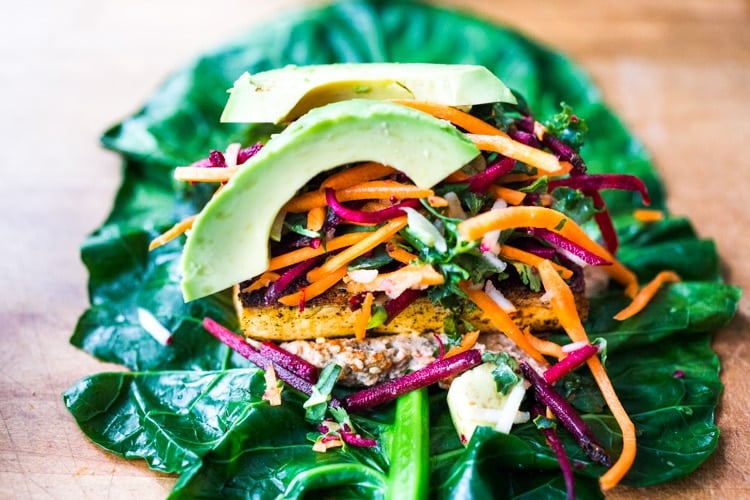 Rainbow Wraps! This vegan collard greens wraps are filled with hummus, crispy tofu, shredded beets, carrots and avocado! Drizzle with Tahini sauce! A delicious healthy lunch! #eatclean #cleaneating #vegan #veganlunch #rainbowwrap #Wraps #veganwrap #plantbased #collardgreens