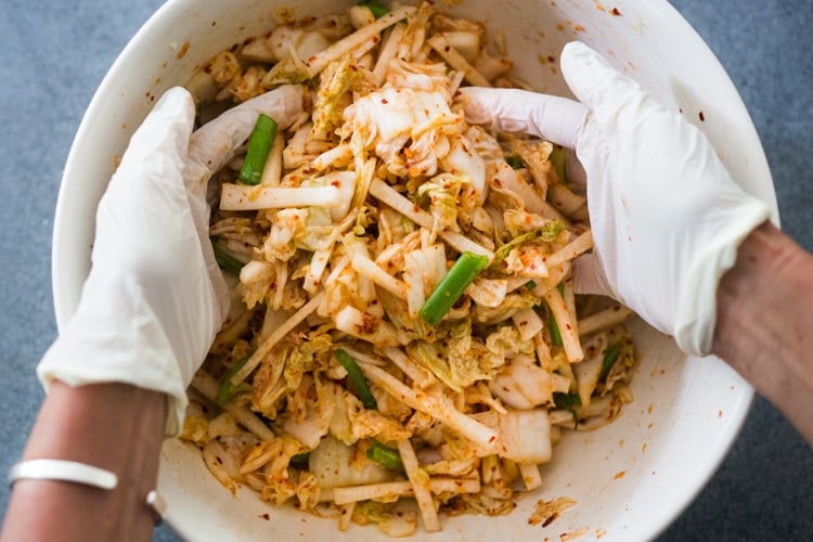Mixing the cabbage with the kimchi paste, scallions and daikon, massaging the cabbage with gloved hands. 