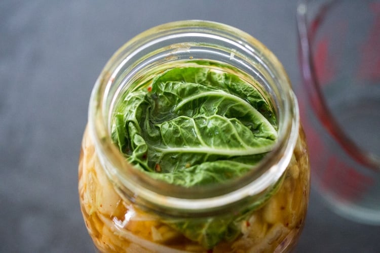 placing a cabbage leaf over the kimchi to weigh it down. 