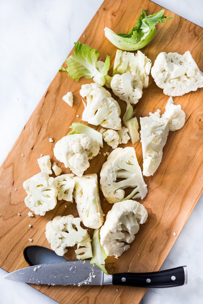 sharp knife and pieces of chopped cauliflower on wood board.