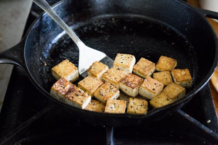 cast iron skillet with cubed tofu, crispy and golden, and metal spatula.