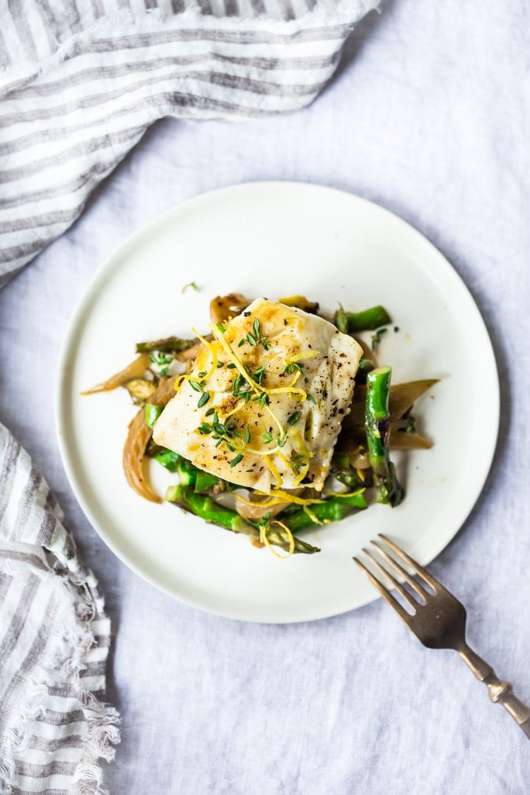 Healthy delicious Baked Cod Recipe with lemon, garlic and thyme, nestled in Spring vegetables- Asparagus, Fennel and Leeks. Simple & Easy. #cod #codrecipe 
