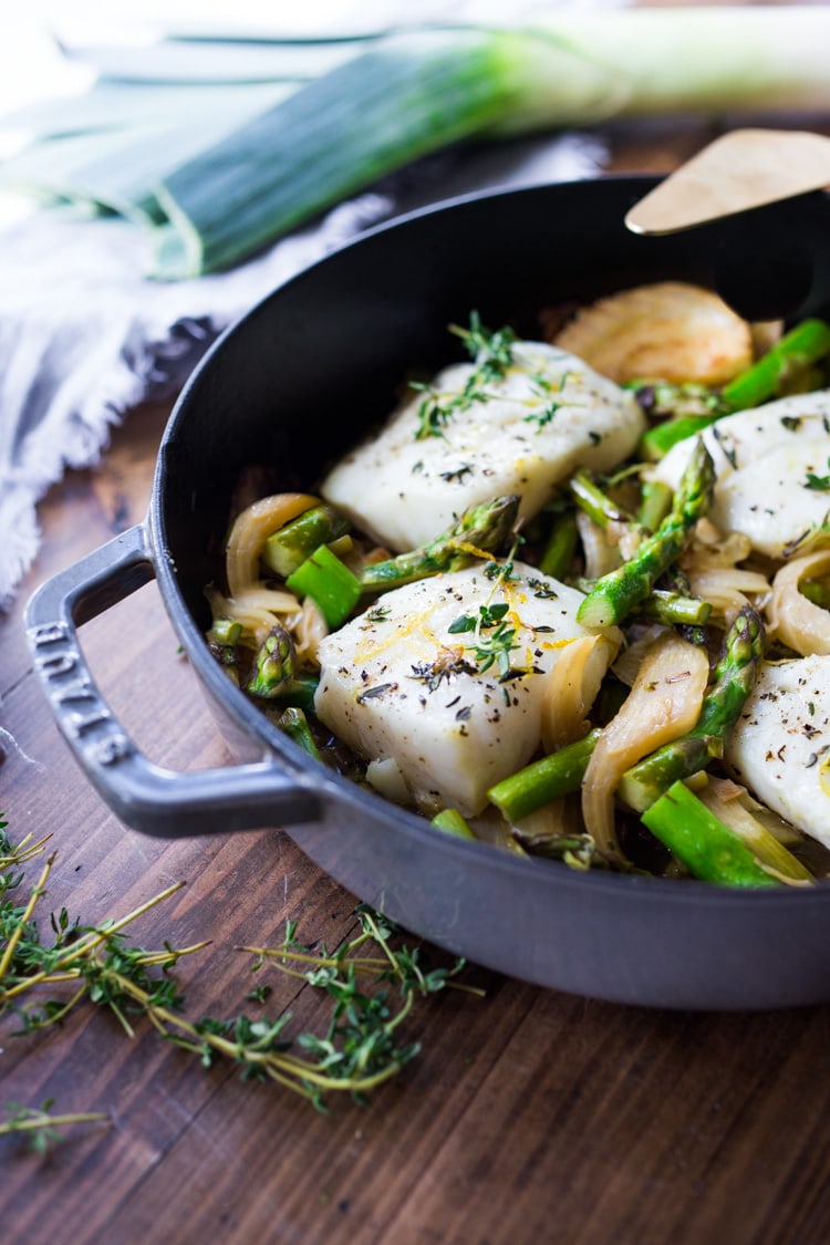 Healthy delicious Baked Cod Recipe with lemon, garlic and thyme, nestled in Spring vegetables- Asparagus, Fennel and Leeks. Simple & Easy. #cod #codrecipe 