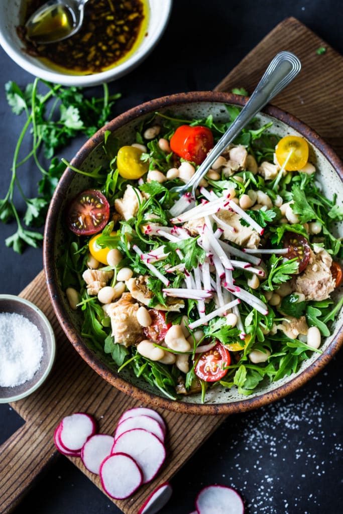 Tuscan tuna salad with arugula and white beans and cherry tomatoes and sliced radish in bowl with fork, a high fiber high protein recipe.