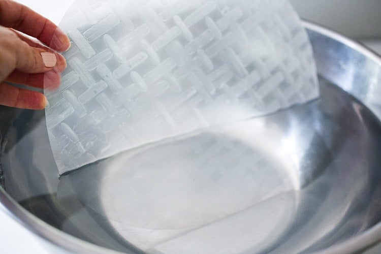 hand dipping rice paper in large bowl of water.