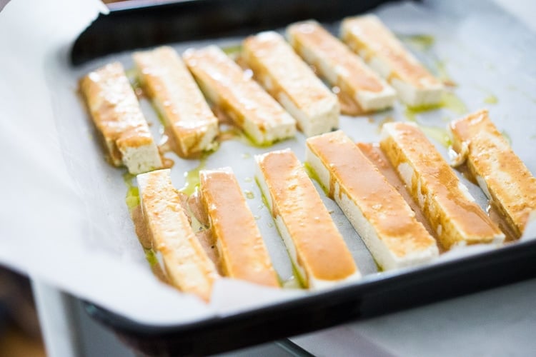 strips of tofu covered in sesame ginger sauce on parchment-lined baking sheet.