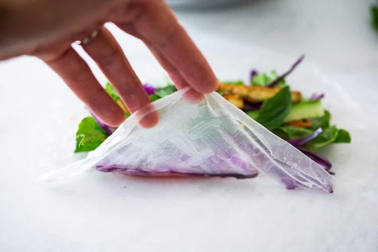hand folding rice paper wrapper over arranged veggies and tofu.