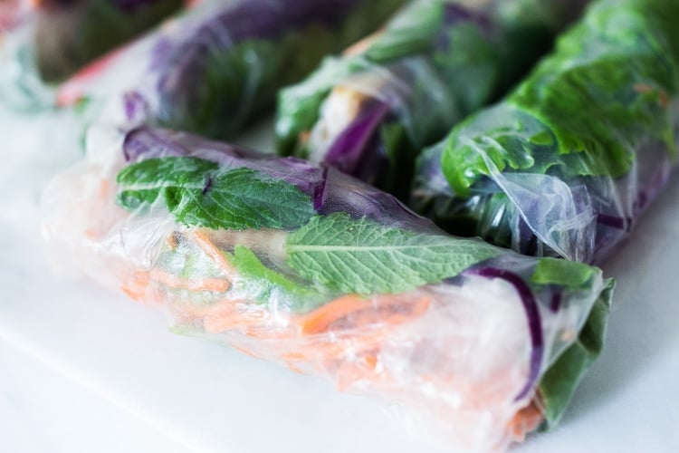 wrapped spring rolls with colorful veggies and herbs visible beneath wrapper.