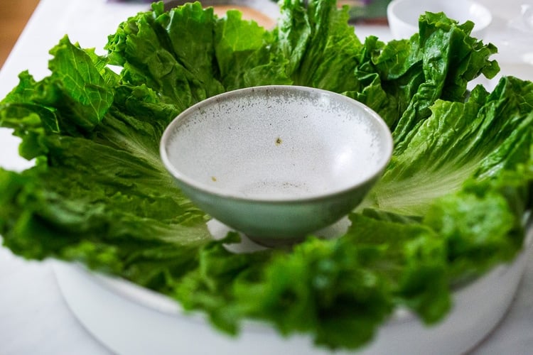 round platter topped with fresh green lettuce and a small bowl in center.