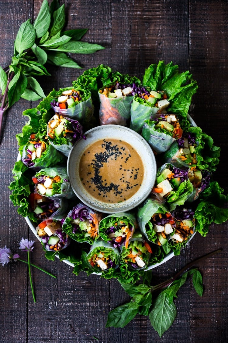 round platter of fresh spring rolls with bowl of peanut sauce in center.