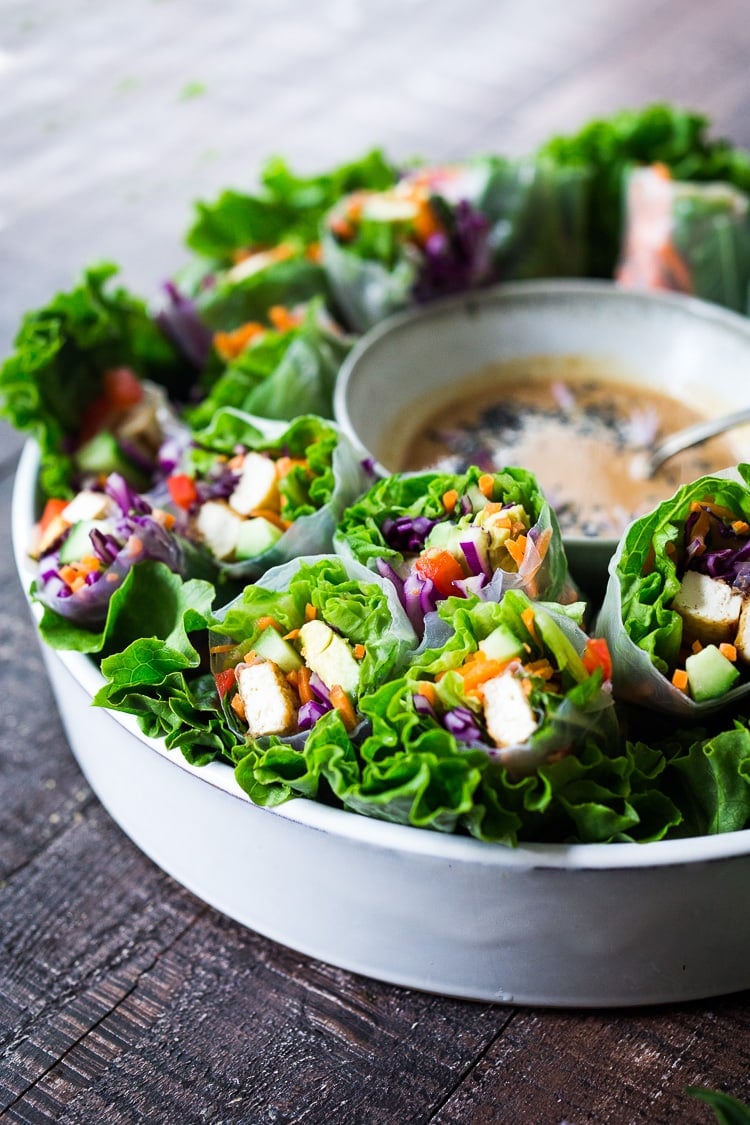 round platter with cut fresh spring rolls showing baked tofu and colorful veggies and a bowl of peanut sauce in center.