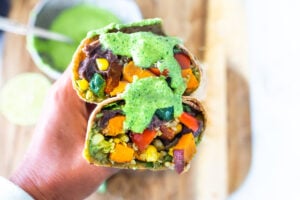 These Vegan Peruvian Burritos are filled with roasted sweet potato, fresh corn, peppers, quinoa and creamy blackbeans, then drizzled with spicy Peruvian Green Sauce. A flavor bomb! Vegan and Delicious! #vegan #burrito #peruvianfood #peruvianrecipes #veganburrito