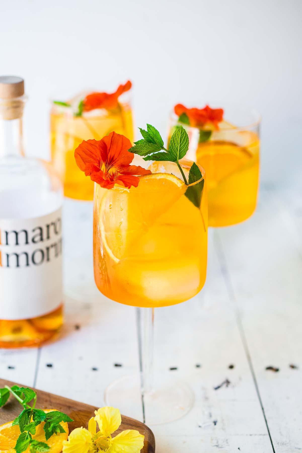 Two Aperol spritz with a bottle Amaro, garnish with pretty flowers and mint. In a stemmed glass.
