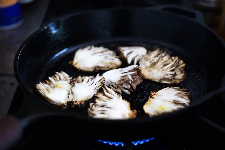 sliced maitake mushrooms pan searing in cast iron skillet.