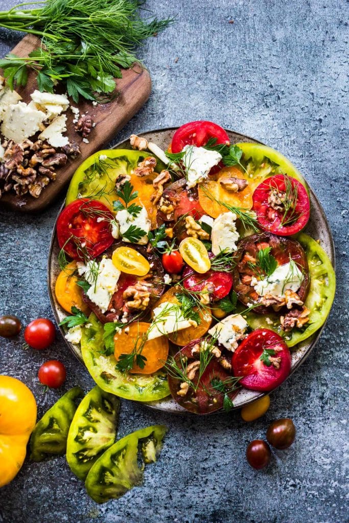 plate of tomato salad with toasted walnuts and smoked blue cheese, garnished with fresh herbs. 