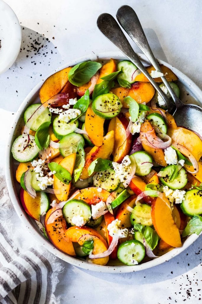 Cucumber Nectarine salad in a white pottery bowl with serving spoons.
