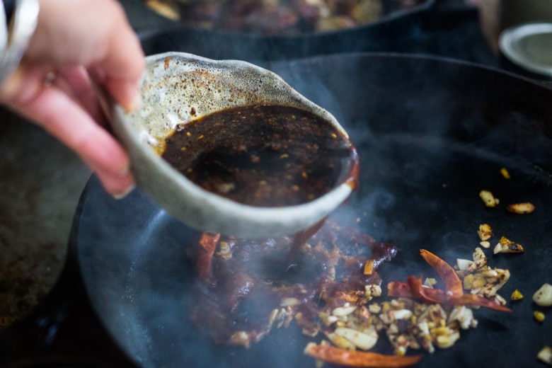 Adding Szechuan sauce, chilies to Chinese eggplant in the skillet.