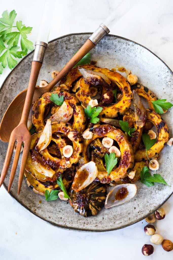 Roasted Delicata Squash with shallots, hazelnuts and Maple Glaze. A tasty vegan side dish perfect for the holiday table. #veganside #delicatasquash #roastedwintersquash #delicata