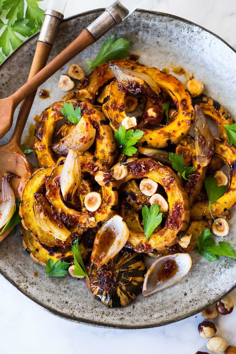 Roasted Delicata Squash with shallots, hazelnuts and Maple Glaze. A tasty vegan side dish perfect for the holiday table. #veganside #delicatasquash #roastedwintersquash #delicata