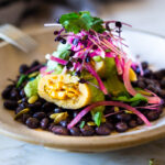 Butternut Tamales with flavorful Pumpkin Seed-Cilantro Sauce over a bed of seasoned black beans, topped with pickled onions and crunchy radishes! A flavorful vegetarian dinner. Vegan adaptable! Can be made ahead!