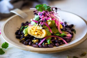 Butternut Tamales with flavorful Pumpkin Seed-Cilantro Sauce over a bed of seasoned black beans, topped with pickled onions and crunchy radishes! A flavorful vegetarian dinner. Vegan adaptable! Can be made ahead!