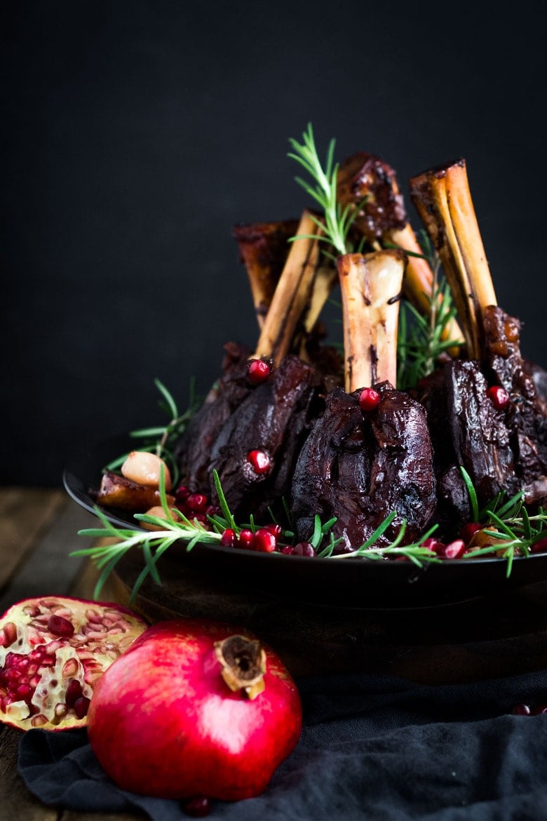 Oven Braised Lamb Shanks with Pomegranate - a festive, Moroccan-inspired lamb recipe that is elegant and delicious! Succulent lamb shanks are roasted in the oven until tender and falling off the bone then drizzled with a falvorful pomegranate sauce.  Serve over creamy soft polenta. #lambshanks #moroccanlamb #braisedlamb #lambrecipes #bakedlamb #lambrecipes #lamb
