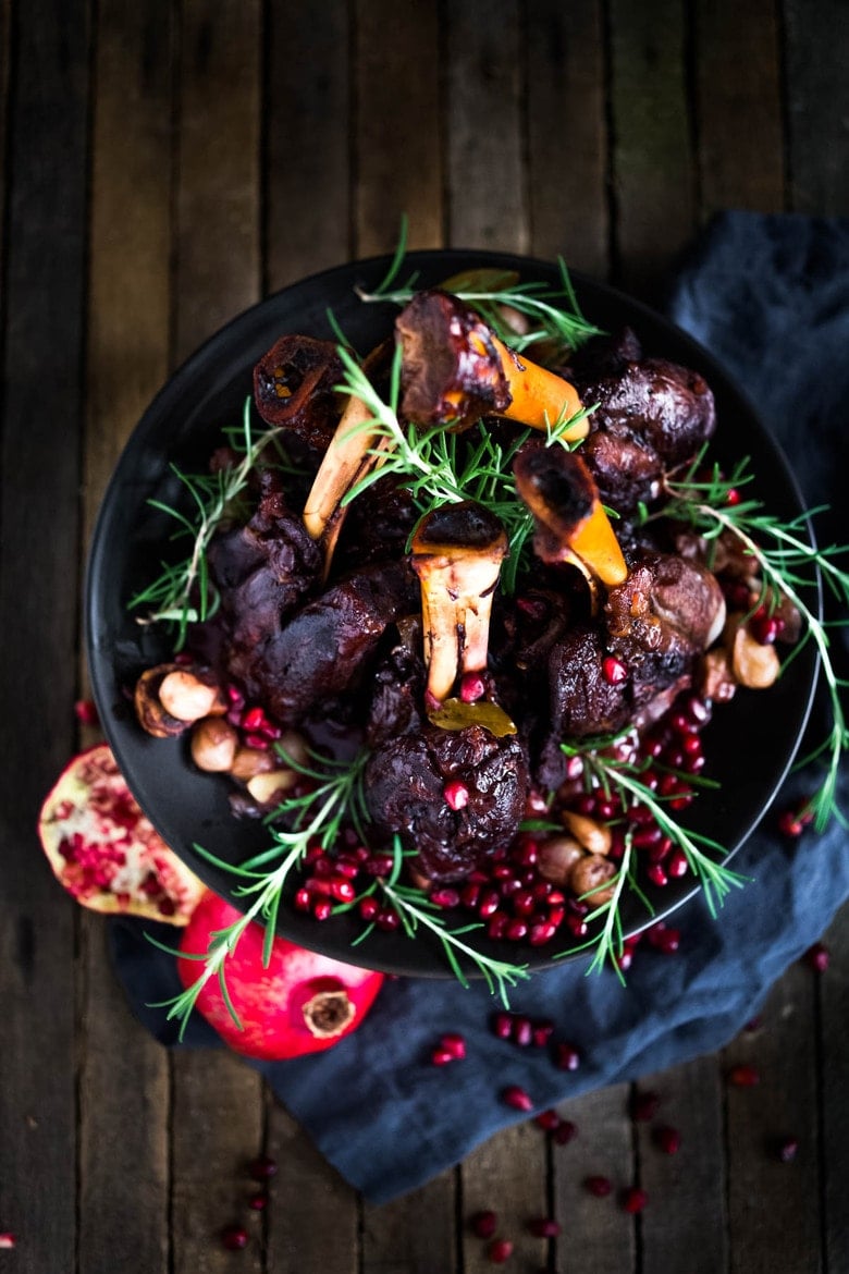 Oven Braised Lamb Shanks with Pomegranate - a festive, Moroccan-inspired lamb recipe that is elegant and delicious! Succulent lamb shanks are roasted in the oven until tender and falling off the bone then drizzled with a falvorful pomegranate sauce.  Serve over creamy soft polenta. #lambshanks #moroccanlamb #braisedlamb #lambrecipes #bakedlamb #lambrecipes #lamb