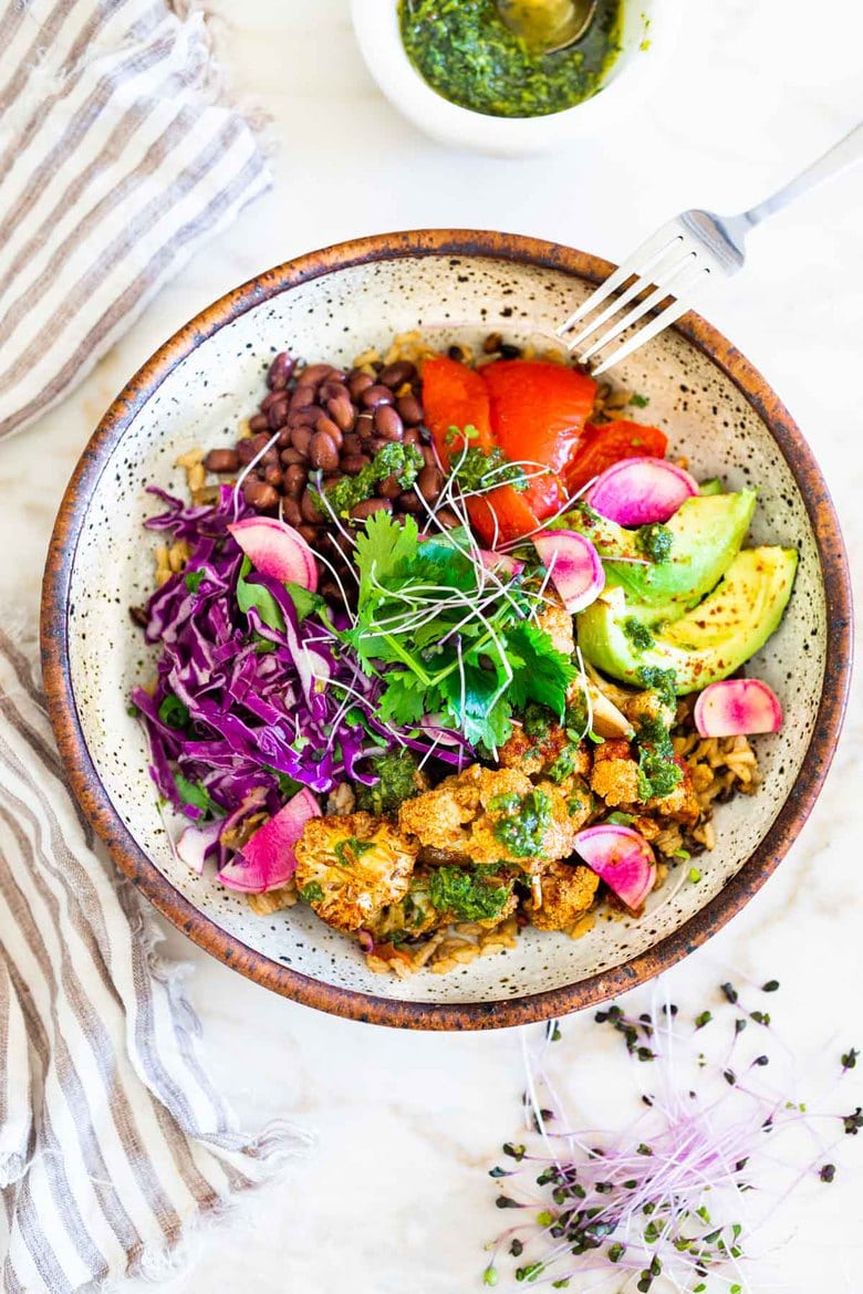 Smokey Cauliflower Chimichurri Bowls!  These filling vegan bowls are full of flavor and loaded up with healthy veggies. Served over seasoned black beans (and optional rice) with Mexican Slaw, radishes, avocado, cilantro and pickled onions. #roastedcauliflower #bowls #veganbowls #veganrecipes #buddhabowls #chimichurri #eatclean #cleaneating #plantbased #healthybowls