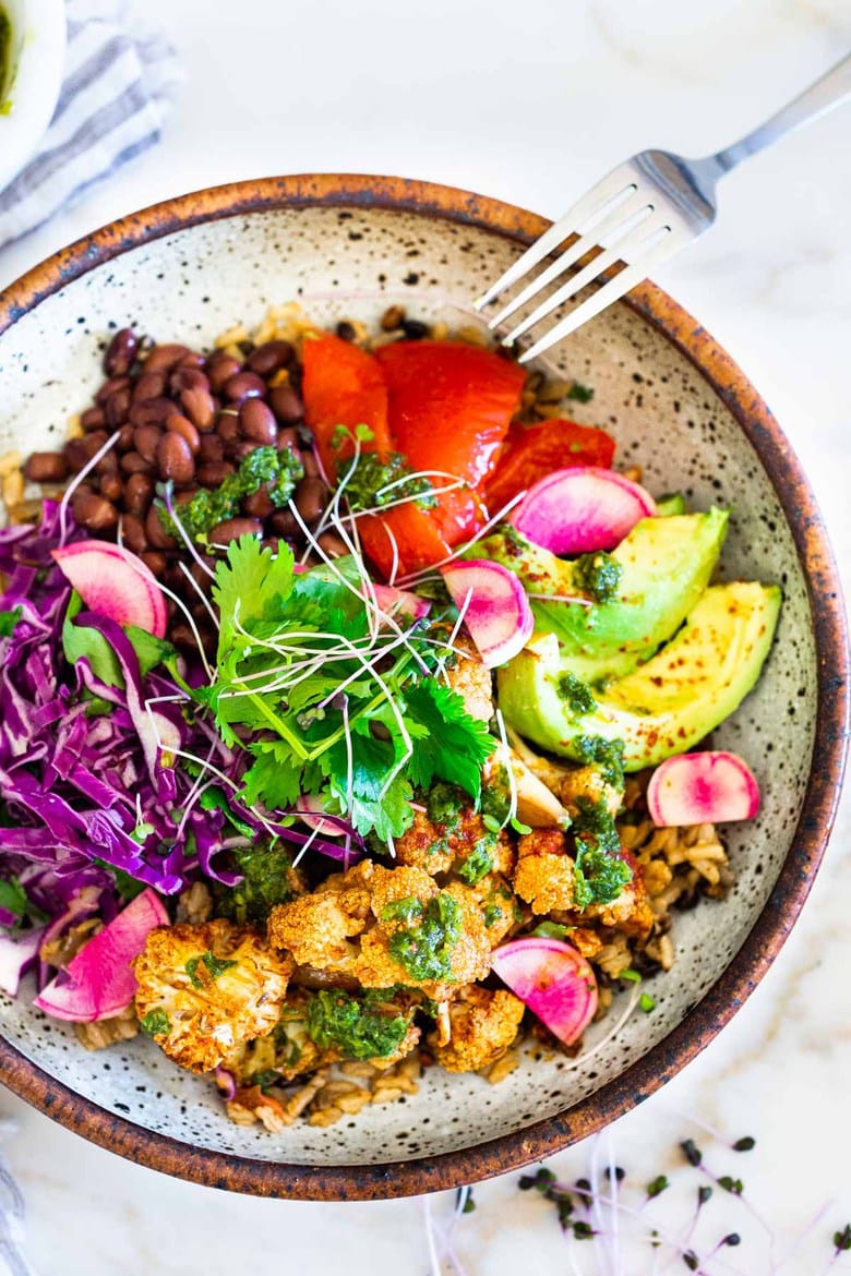 Smokey Cauliflower Chimichurri Bowls!  These filling vegan bowls are full of flavor and loaded up with healthy veggies. Served over seasoned black beans (and optional rice) with Mexican Slaw, radishes, avocado, cilantro and pickled onions. #roastedcauliflower #bowls #veganbowls #veganrecipes #buddhabowls #chimichurri #eatclean #cleaneating #plantbased #healthybowls