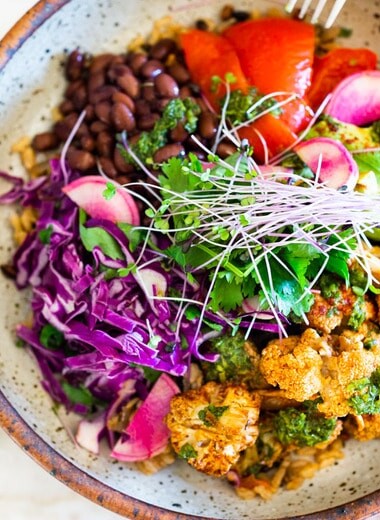 Smokey Cauliflower Chimichurri Bowls!  These filling vegan bowls are full of flavor and loaded up with healthy veggies. Served over seasoned black beans (and optional rice) with Mexican Slaw, radishes, avocado, cilantro and pickled onions. #roastedcauliflower #bowls #veganbowls #veganrecipes #buddhabowls #chimichurri #eatclean #cleaneating #plantbased #healthybowls